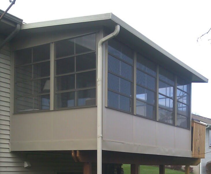 Screened-in porch addition with tan siding and dark screens, attached to a house with a visible wooden deck.