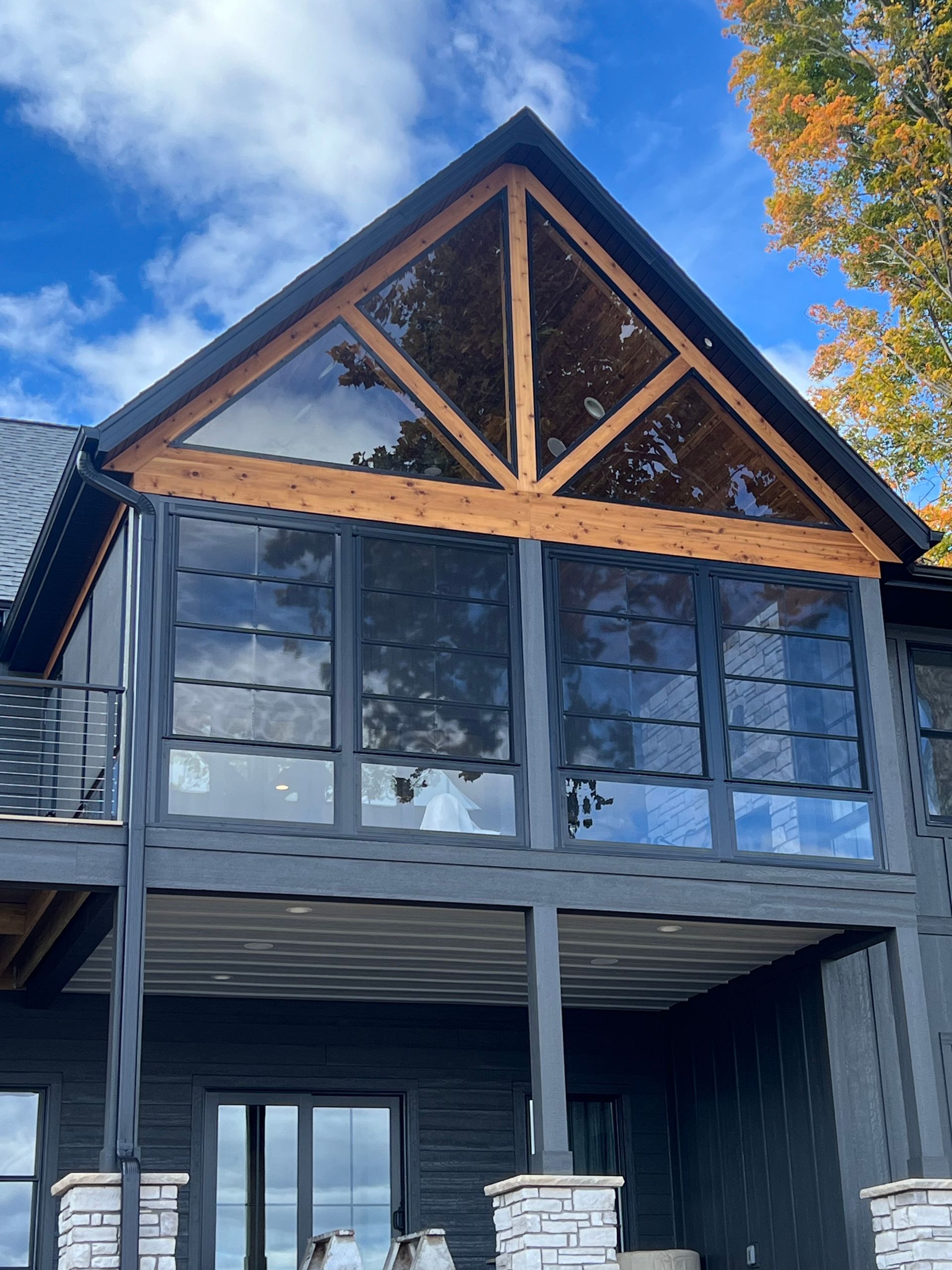 Dark gray house with screened porch and wood beams under blue sky.