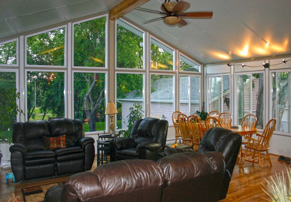 Sunroom with leather furniture, dining table, and large windows overlooking trees.