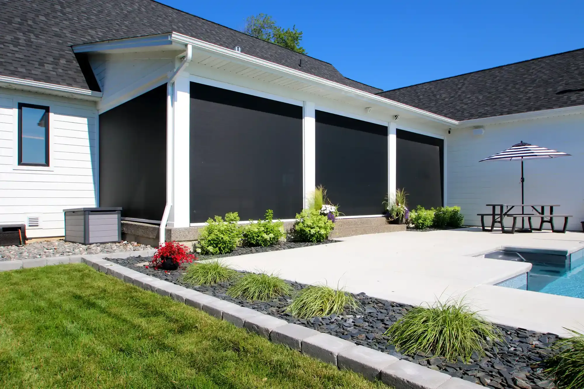 Exterior of a house with black sun shades, a pool, and landscaping.