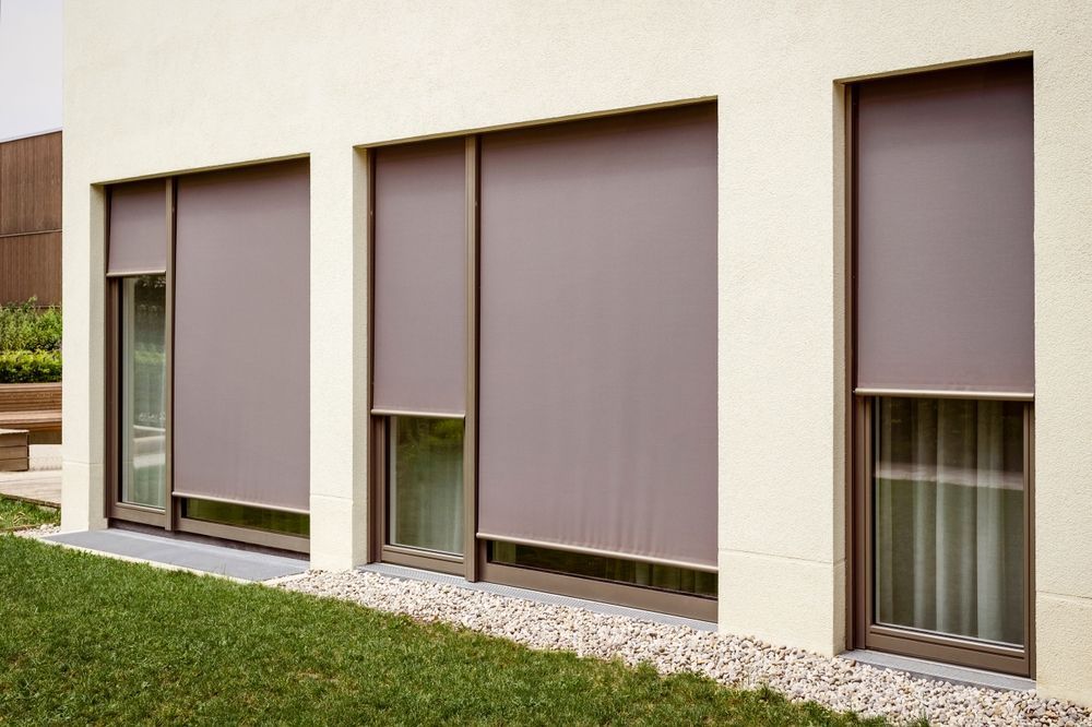 Exterior of a building with three windows, each having a retractable shade pulled down.