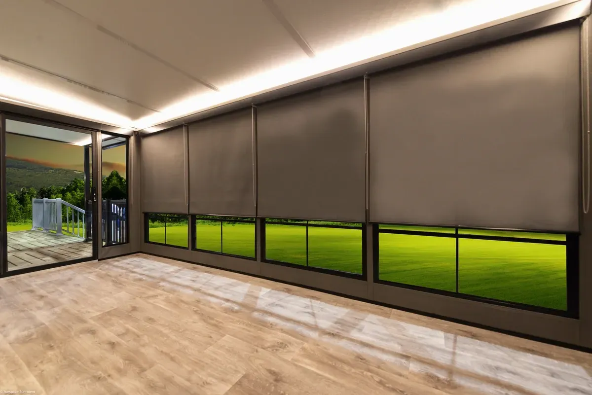 Room with closed gray blinds and open windows revealing a grassy field.