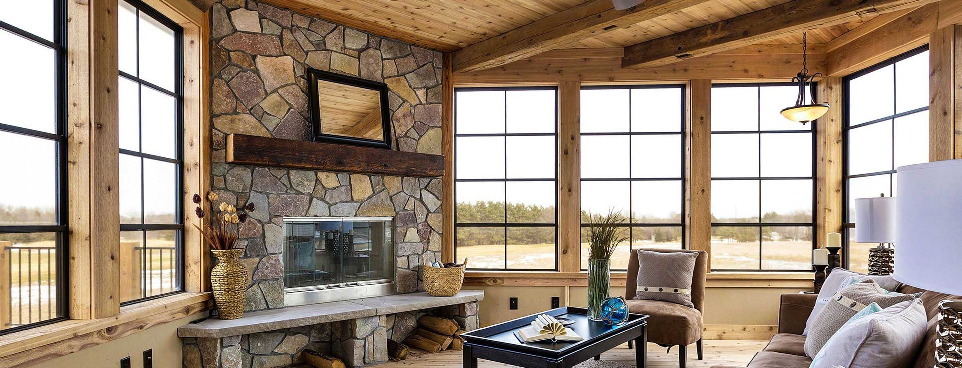 Cozy cabin living room with stone fireplace, large windows, and natural wood beams.