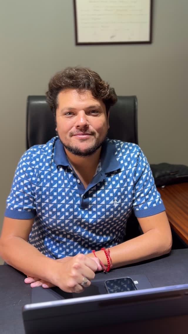 Hombre con camisa azul estampada, sentado en un escritorio, mirando a la cámara.