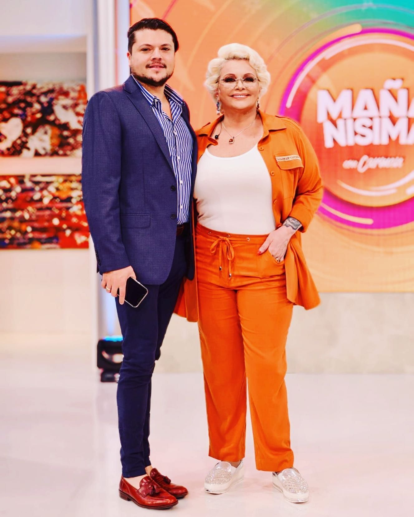 Dos personas, un hombre y una mujer, de pie juntos. La mujer vestida de naranja, el hombre con traje azul.