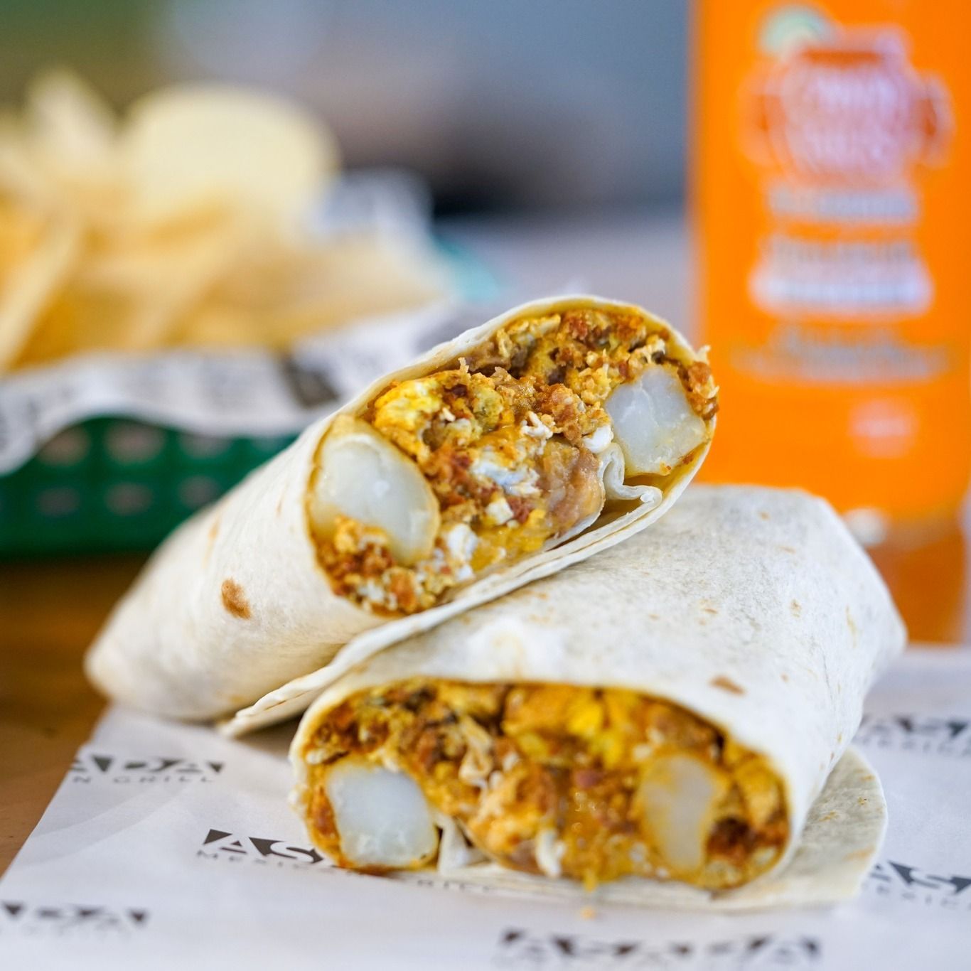 a burrito is sitting on a table next to a bottle of orange juice
