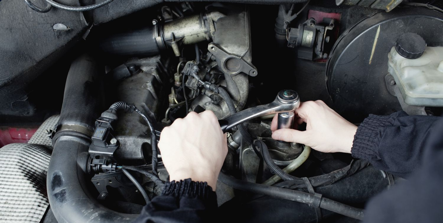 Hands using a wrench to work on a car engine.