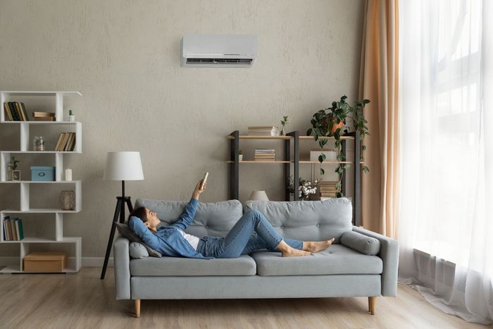 A woman is laying on a couch in a living room holding a remote control.