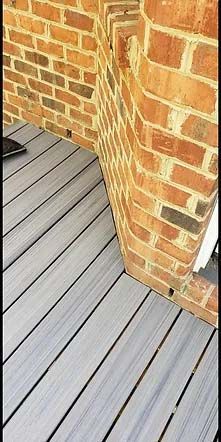 close-up of wooden deck meeting the bottom of a brick wall