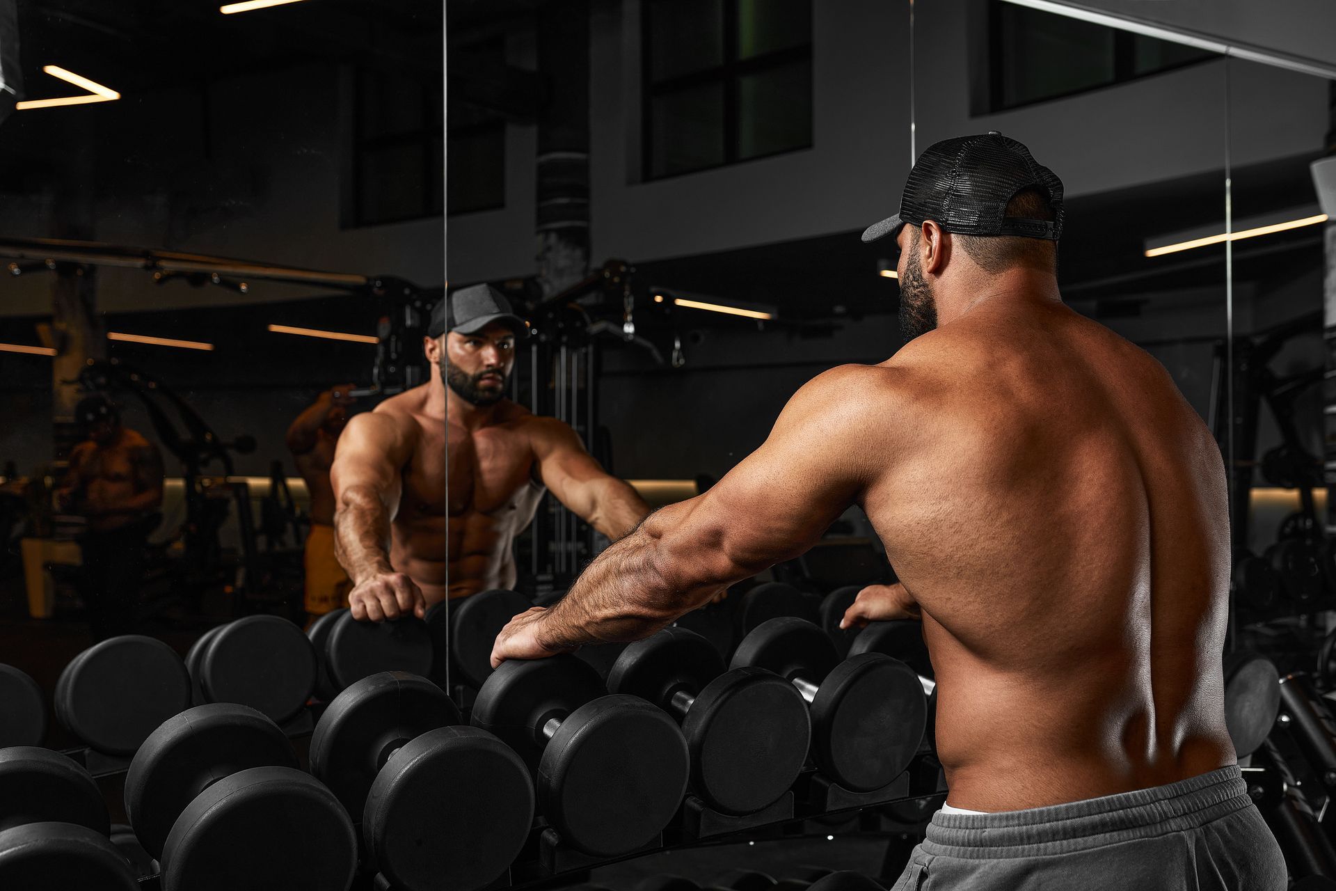 Body builder leaning on dumbbells looking in mirror