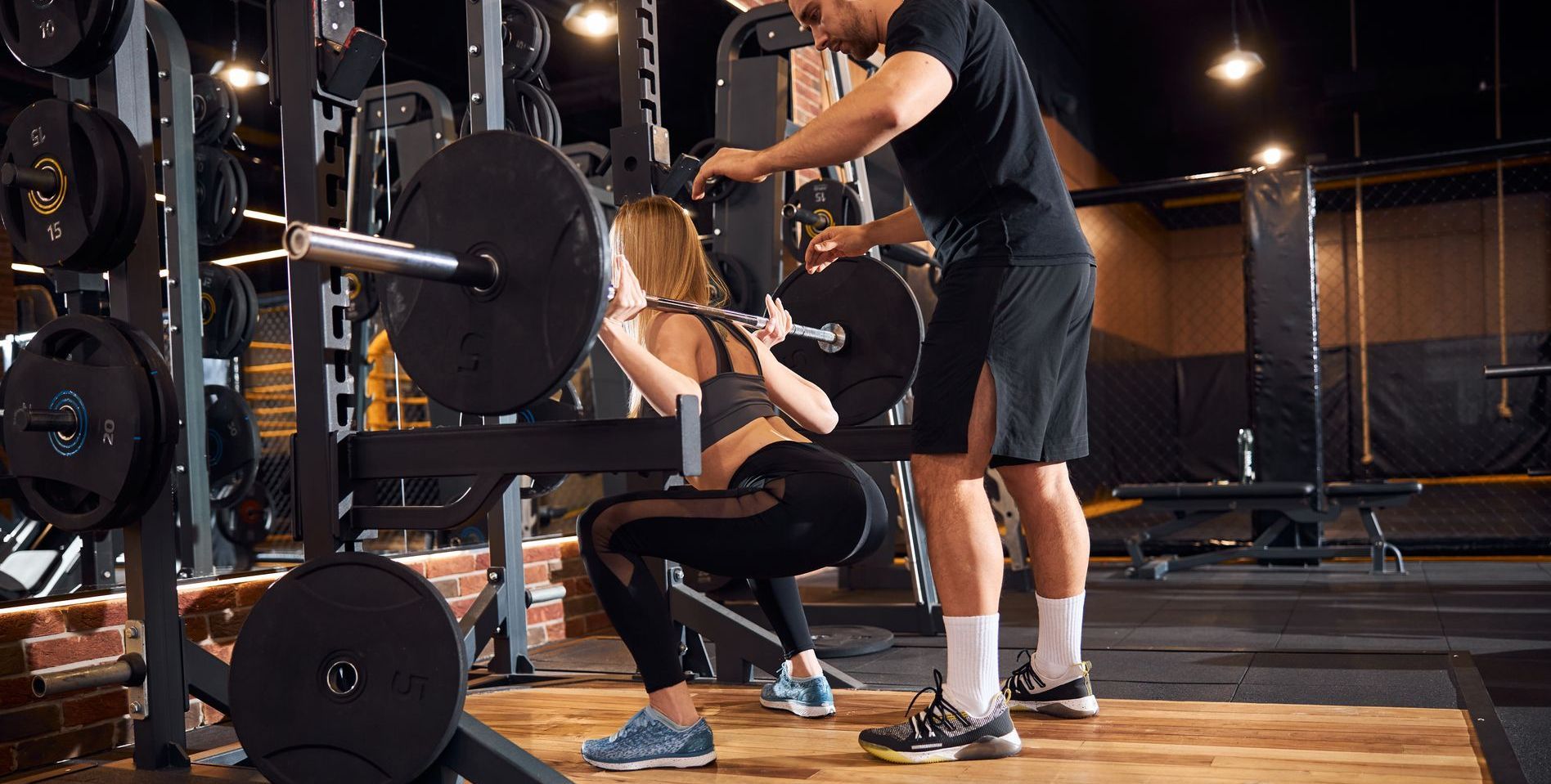 Personal Trainer helping female client squat in a gym