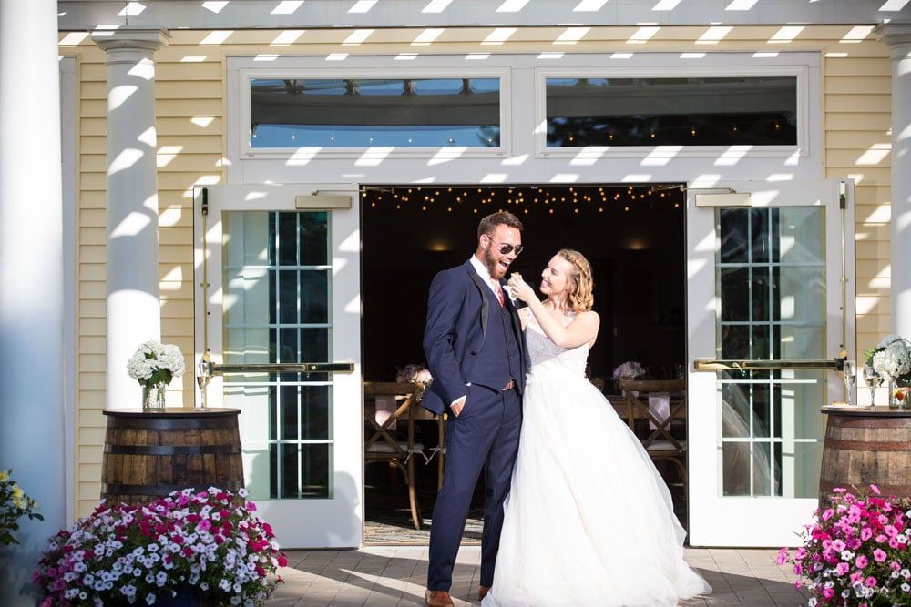 Bride adjusting groom's tie at outdoor wedding entrance, sunny day.