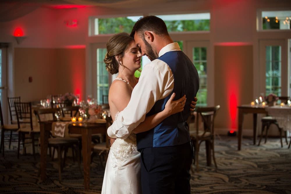 Bride and groom dancing, embracing indoors with red uplighting.