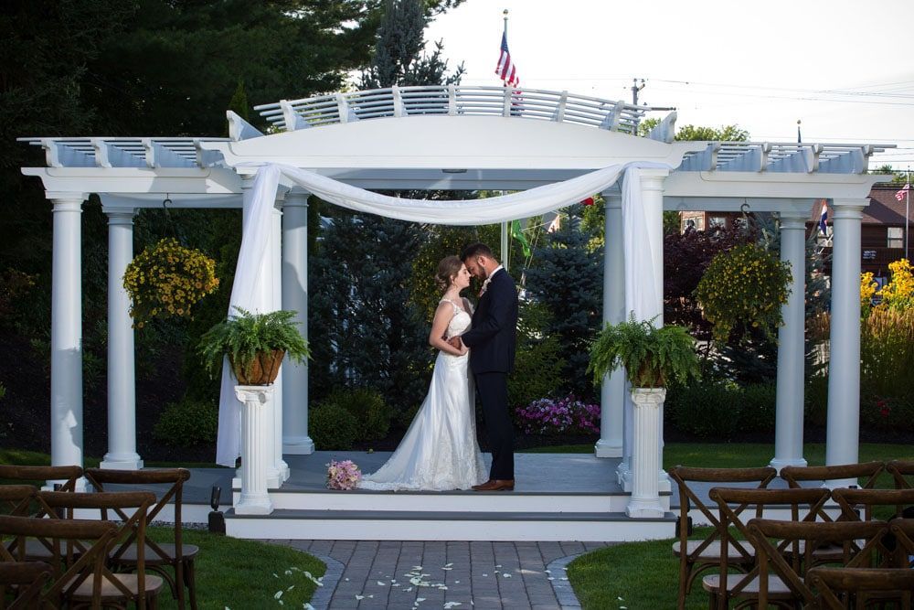 Bride and groom kissing under a white pergola with draped fabric. Outdoor wedding ceremony.