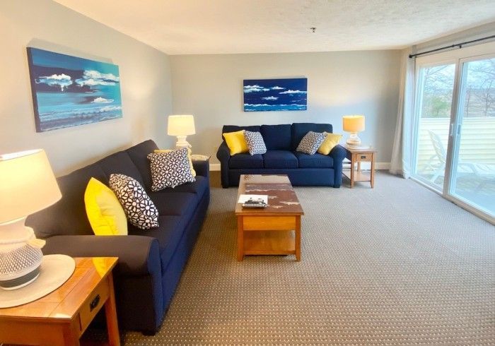 Living room with two navy couches, wood furniture, and sliding glass doors.