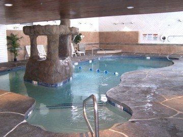 Indoor pool with rock formation, turquoise water, and a stone tile surround.