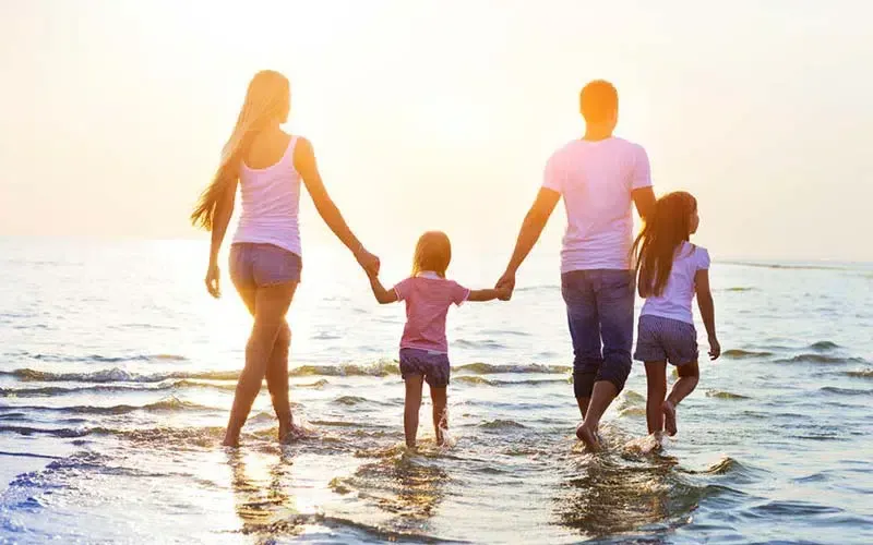 Family of four walking into the ocean at sunset, holding hands.