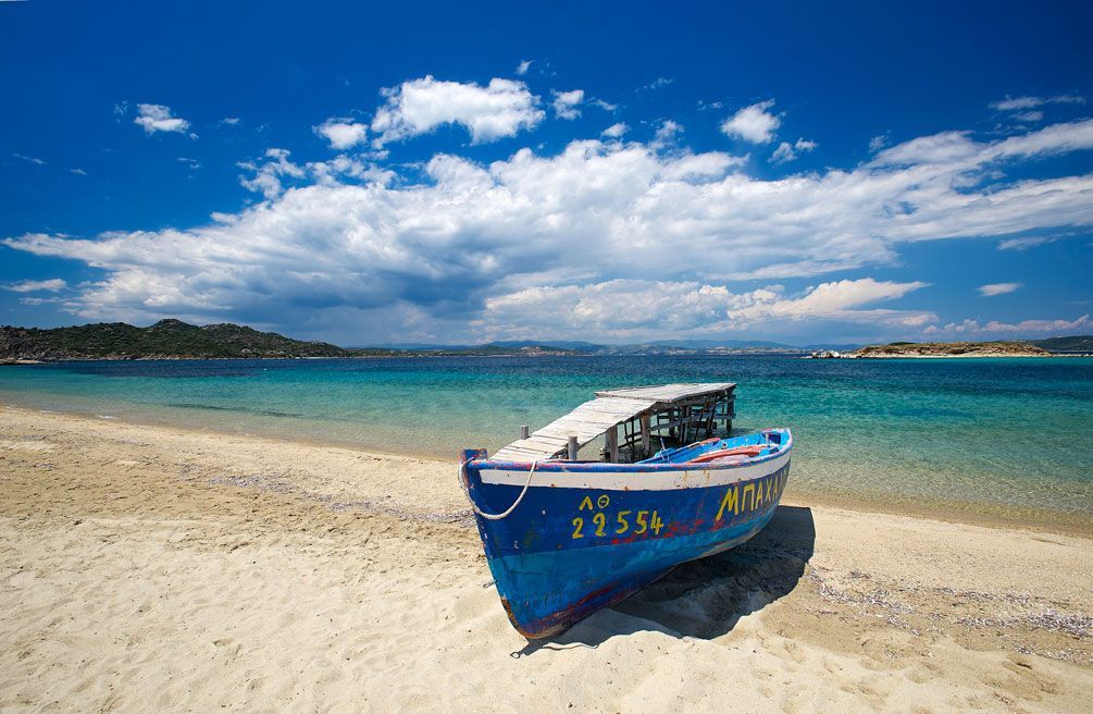 A blue and white boat is sitting on a sandy beach near the ocean.