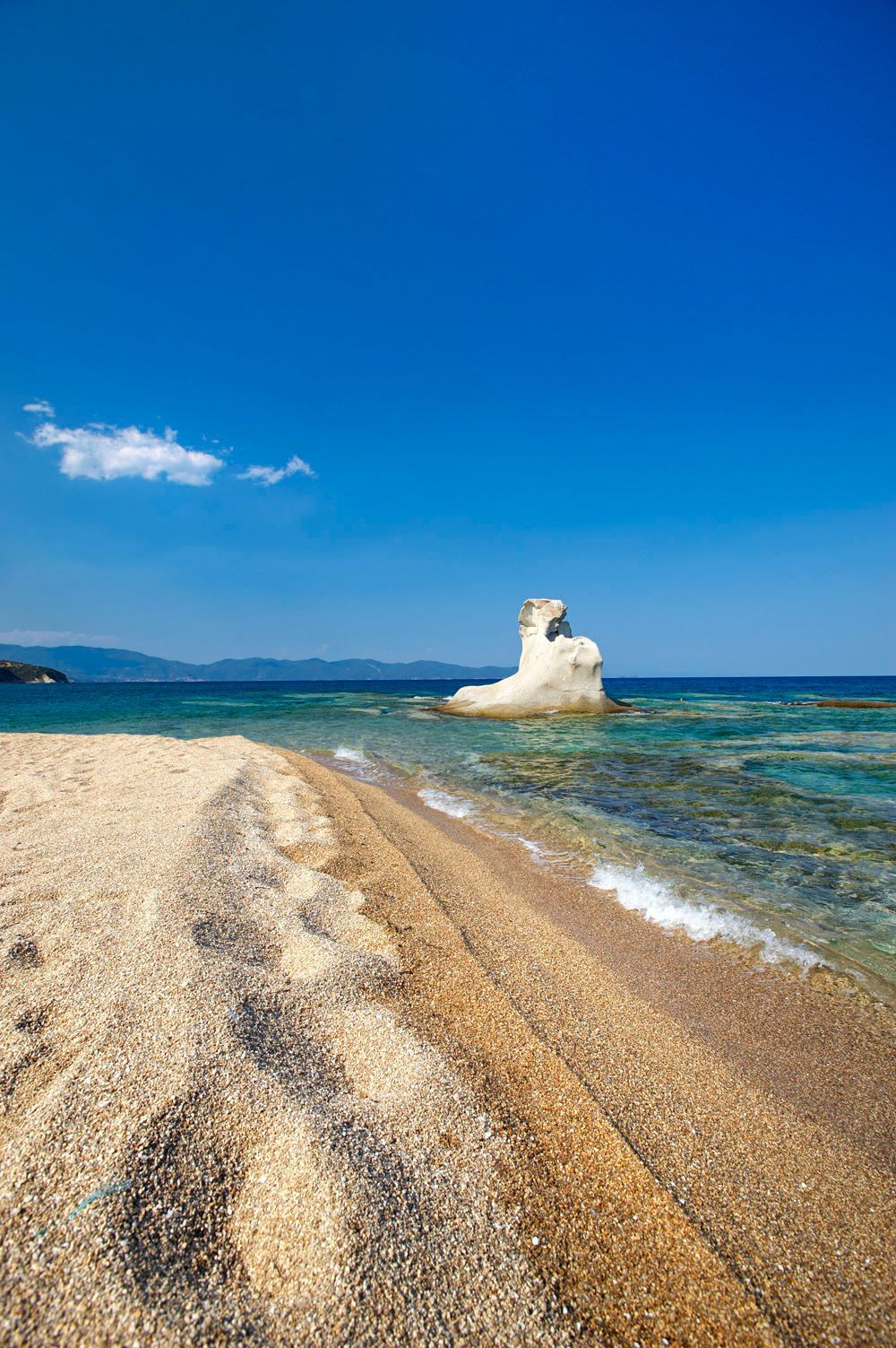 There is a large rock in the middle of the ocean on the beach.