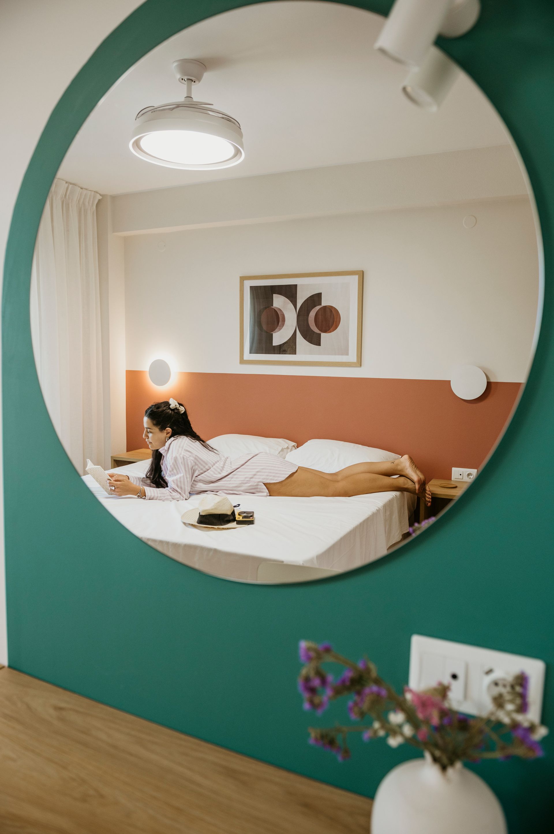 A woman is laying on a bed in front of a large round mirror.