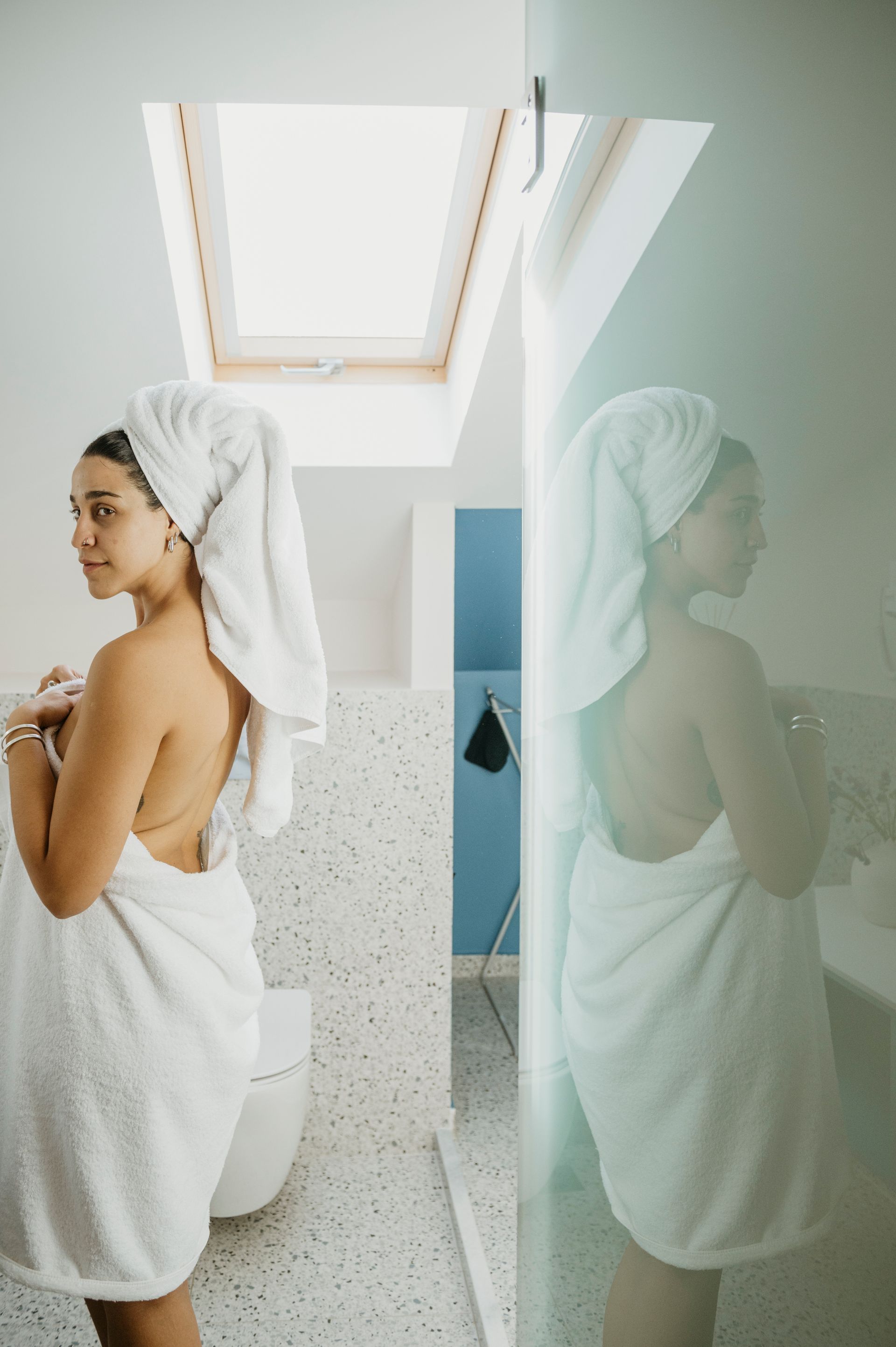 A woman wrapped in a towel is standing in a bathroom next to a toilet.