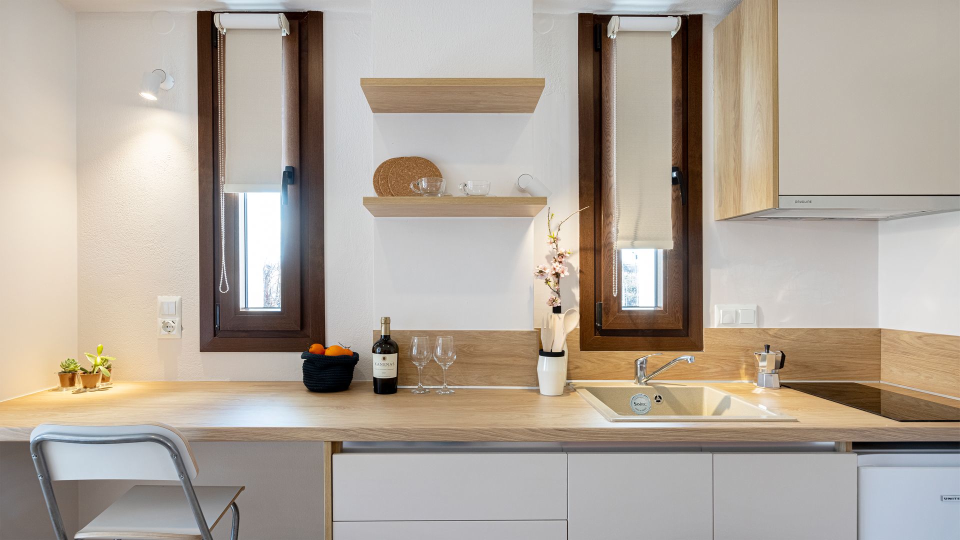 A kitchen with a sink , stove , chair and shelves.