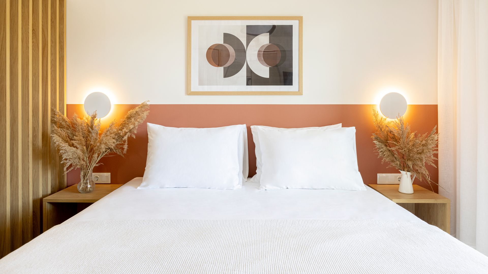 A bed with white sheets and pillows in a bedroom with a picture on the wall above it.