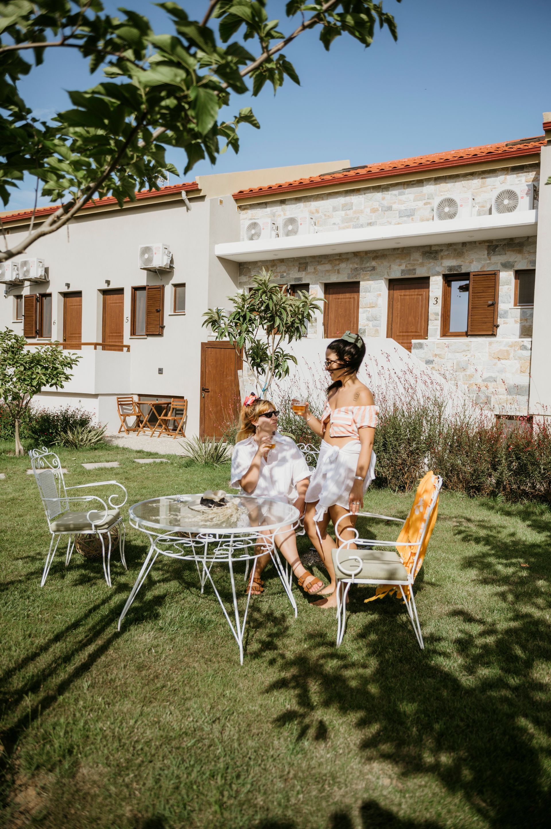 Two women are sitting at a table in a garden in front of a house.
