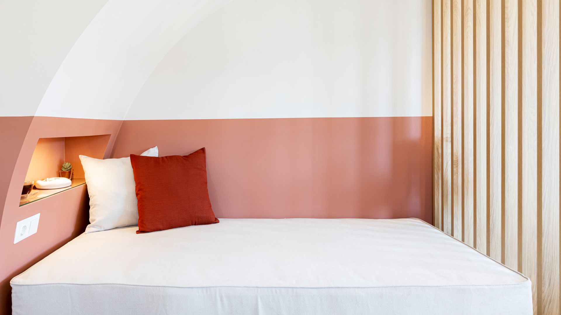 A bed with two pillows on it in a bedroom with a pink wall.