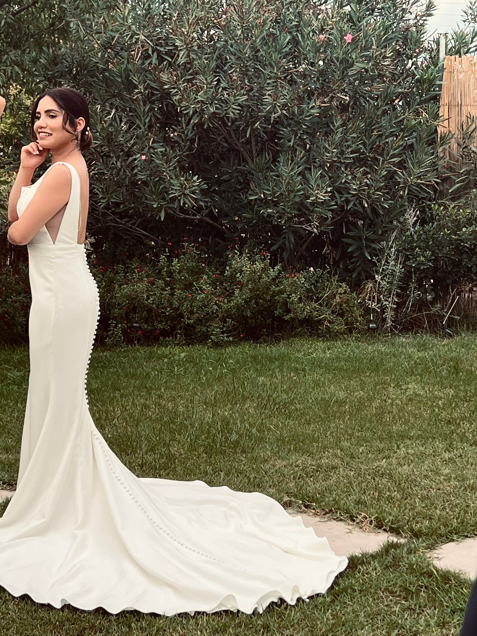 A woman in a white wedding dress is standing in the grass.