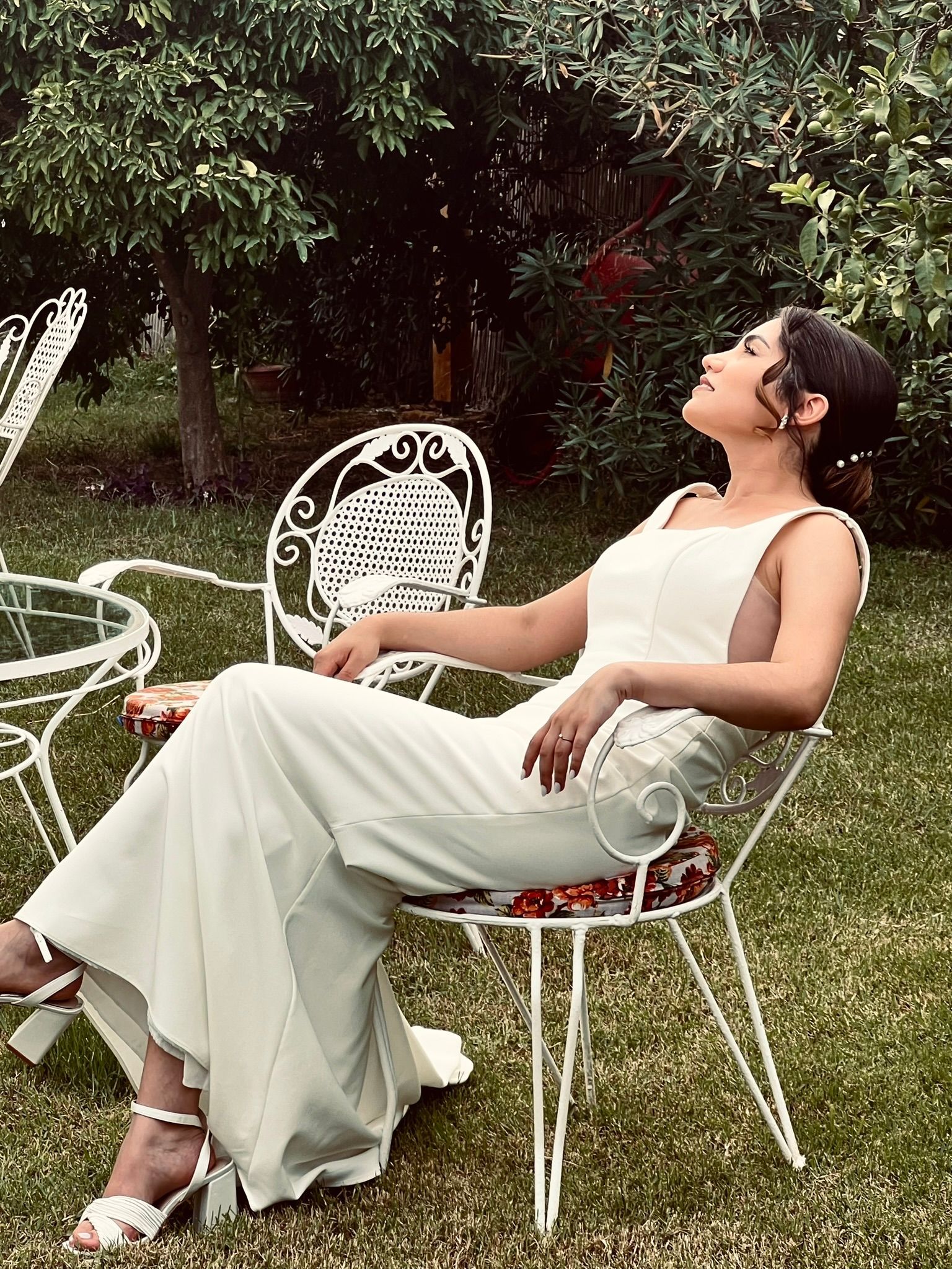 A woman in a white dress is sitting on a chair in the grass.