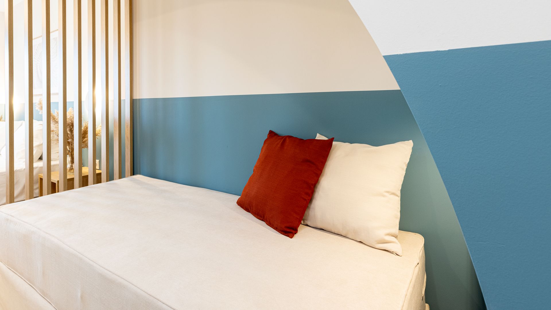 A bed with white sheets and pillows in a room with blue and white walls.