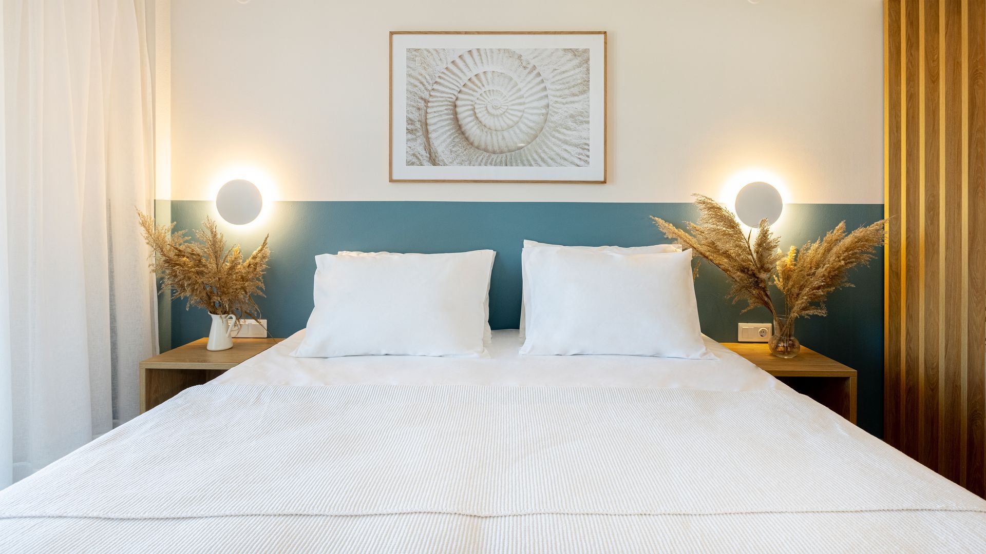 A bed with white sheets and pillows in a bedroom with a picture on the wall above it.