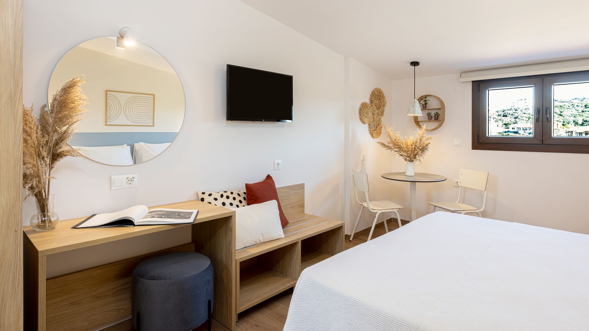 A hotel room with a bed , table , mirror and television.