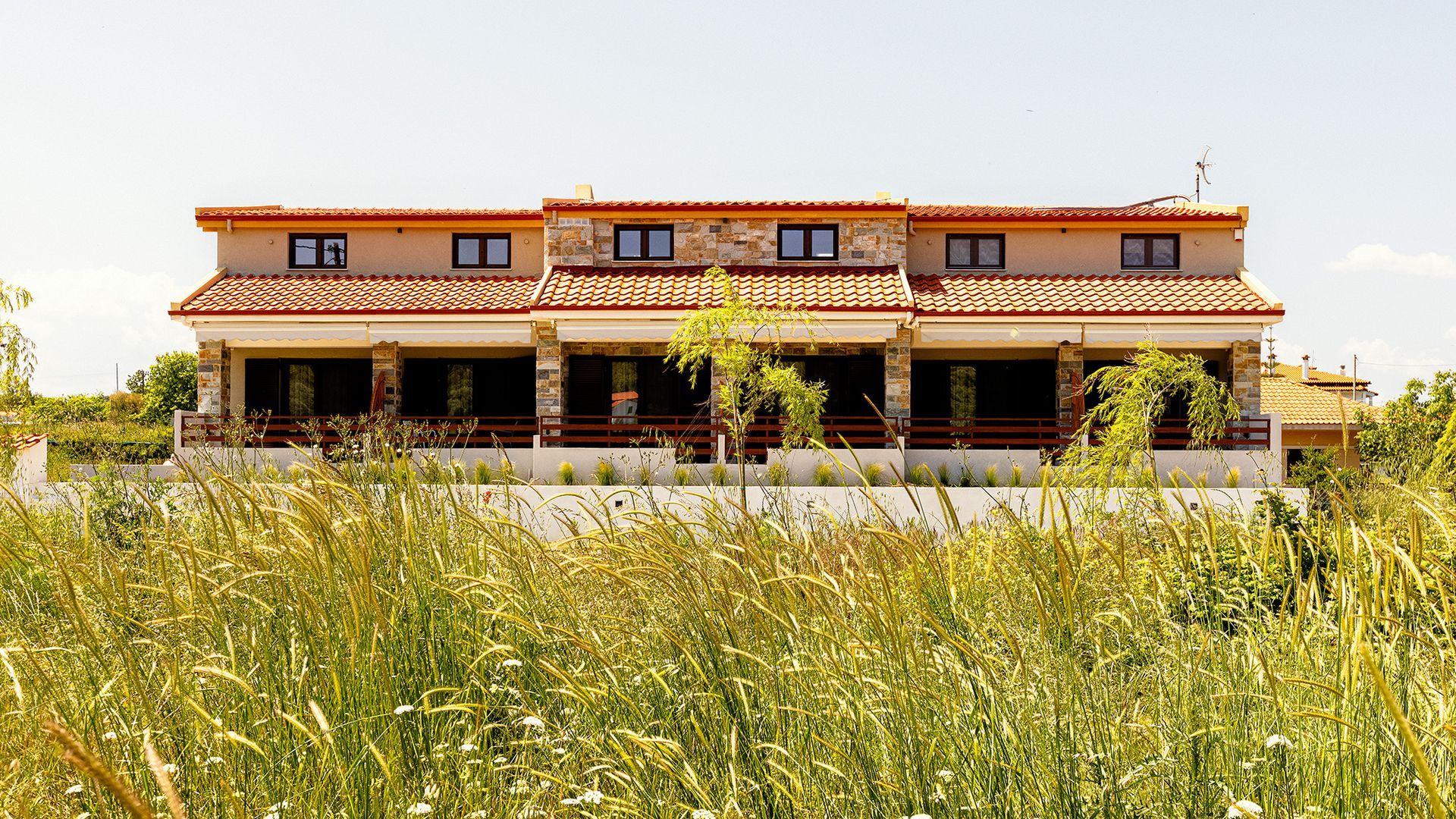 A large house with a red tile roof is surrounded by tall grass.