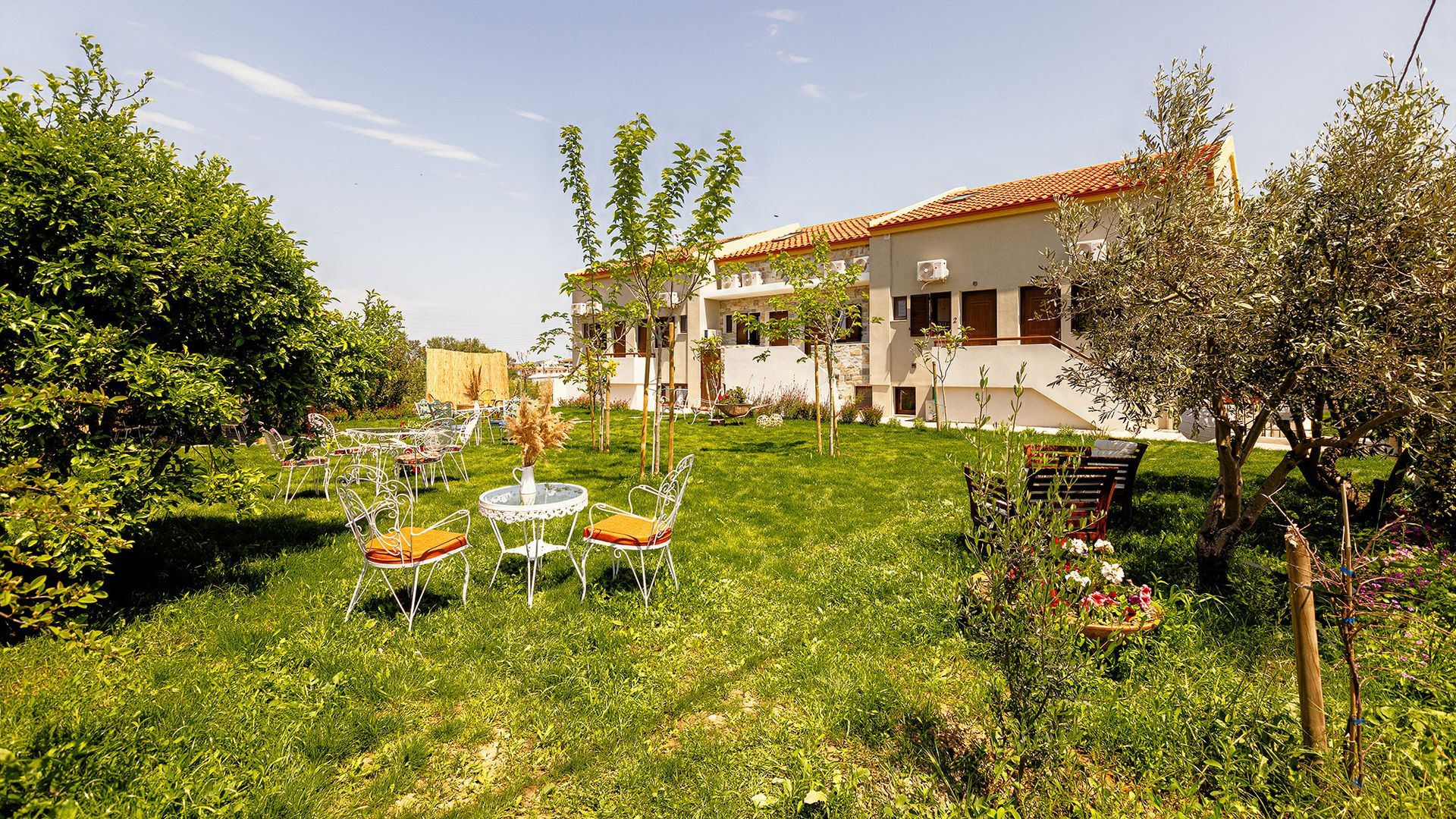 A white house with a red tile roof is surrounded by trees and a lush green lawn.