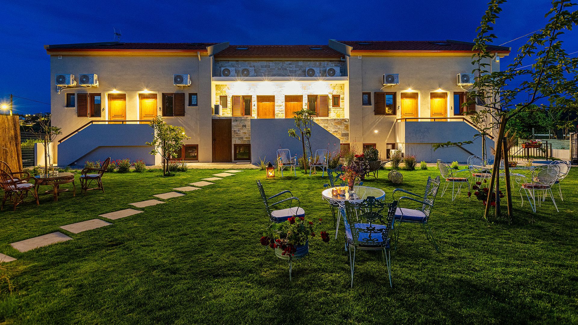 A large white house is lit up at night with tables and chairs in front of it.