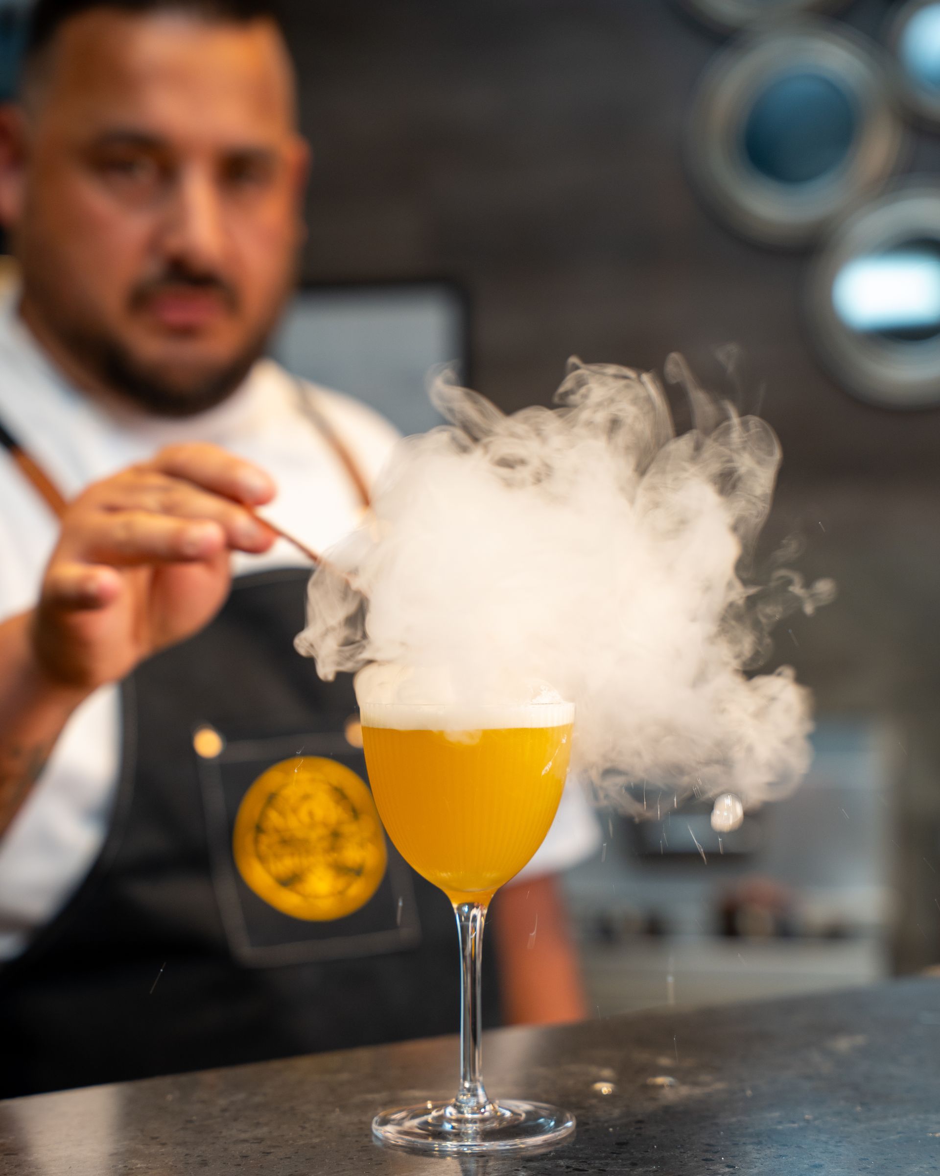 Bartender adds smoke to a yellow cocktail. Smoke billows up from the glass.