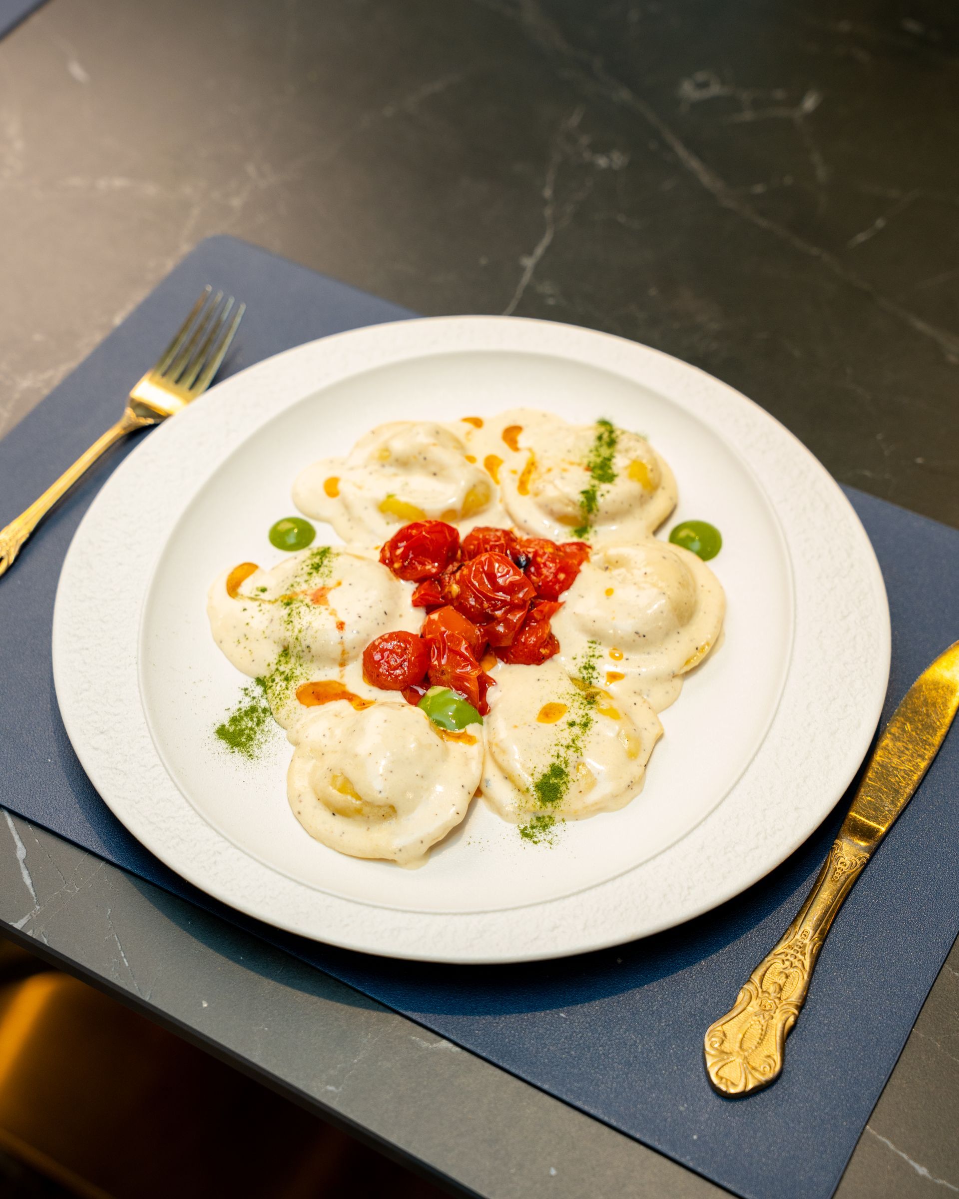 White plate of ravioli with red sauce and green garnish, served with gold cutlery.