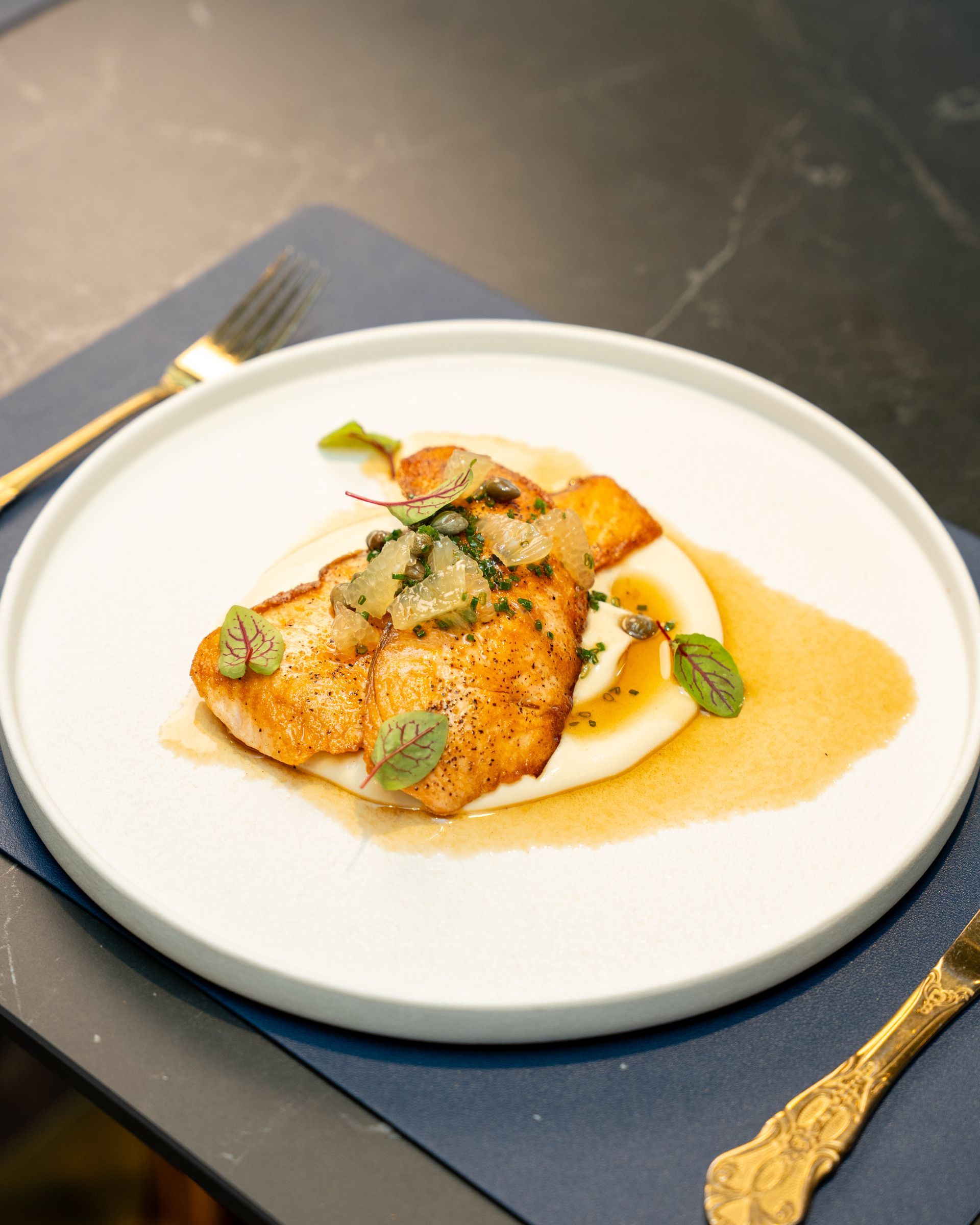 Pan-seared fish with sauce on mashed potatoes, garnished with herbs, plated on white ceramic.