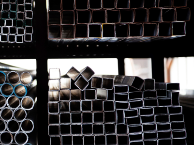 Pilas de tubos metálicos cuadrados y redondos en un almacén.