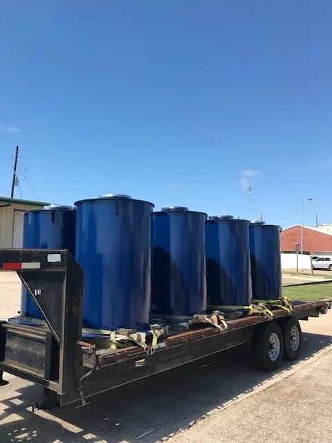 A trailer filled with blue barrels is parked on the side of the road.