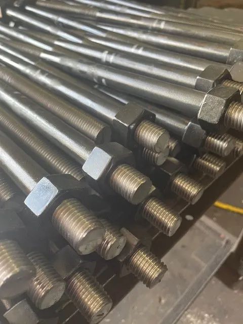 A bunch of metal rods with nuts on them are stacked on top of each other on a table.