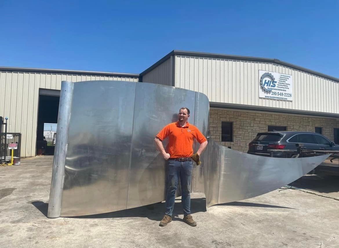 A man in an orange shirt is standing in front of a large piece of metal.