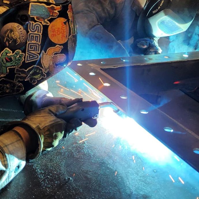A person welding with a sega sticker on their helmet