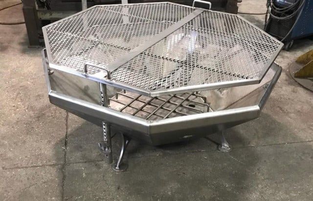 A stainless steel fire pit is sitting on a cement floor.