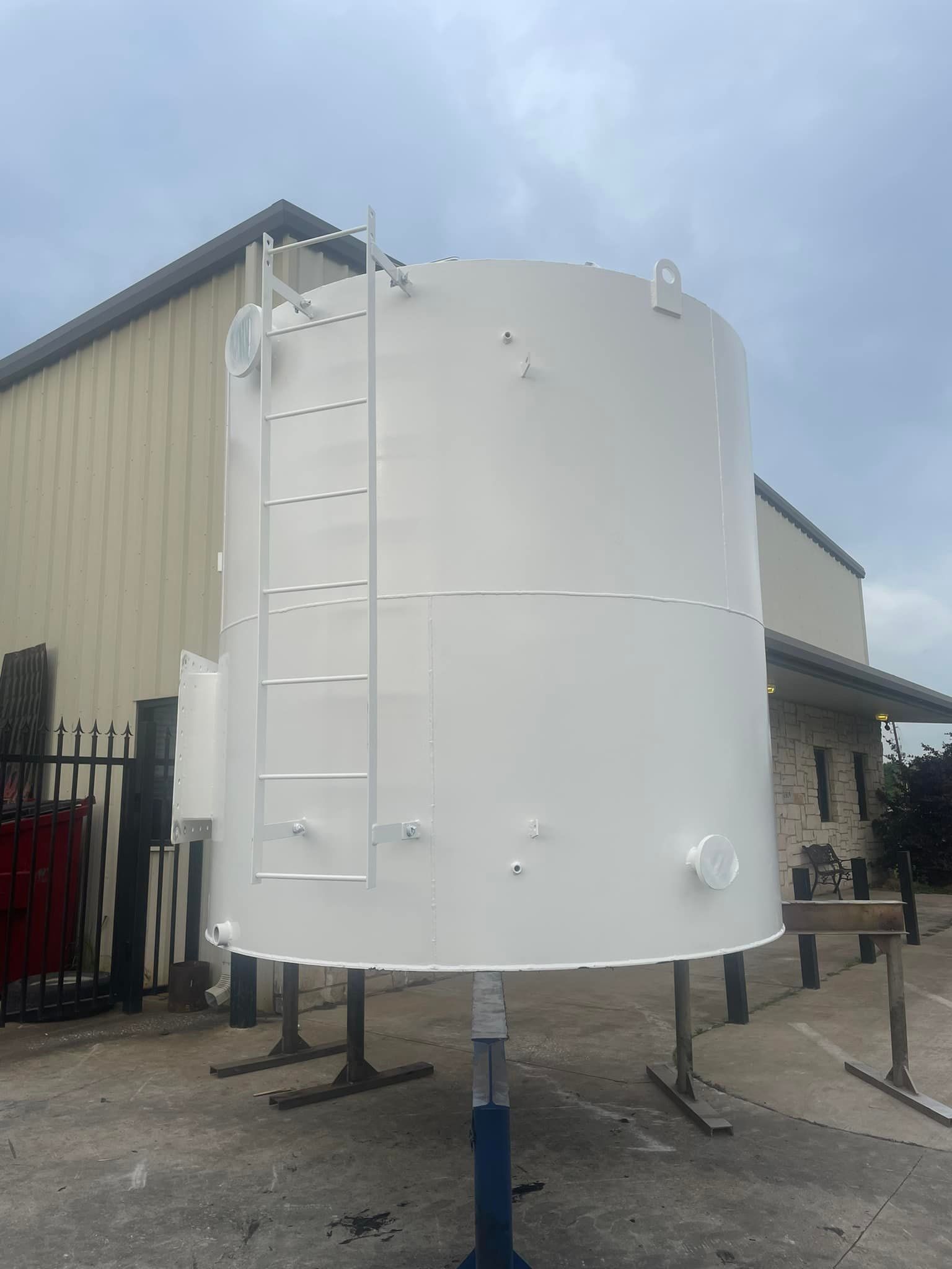 A large white tank with a ladder attached to it is sitting in front of a building.