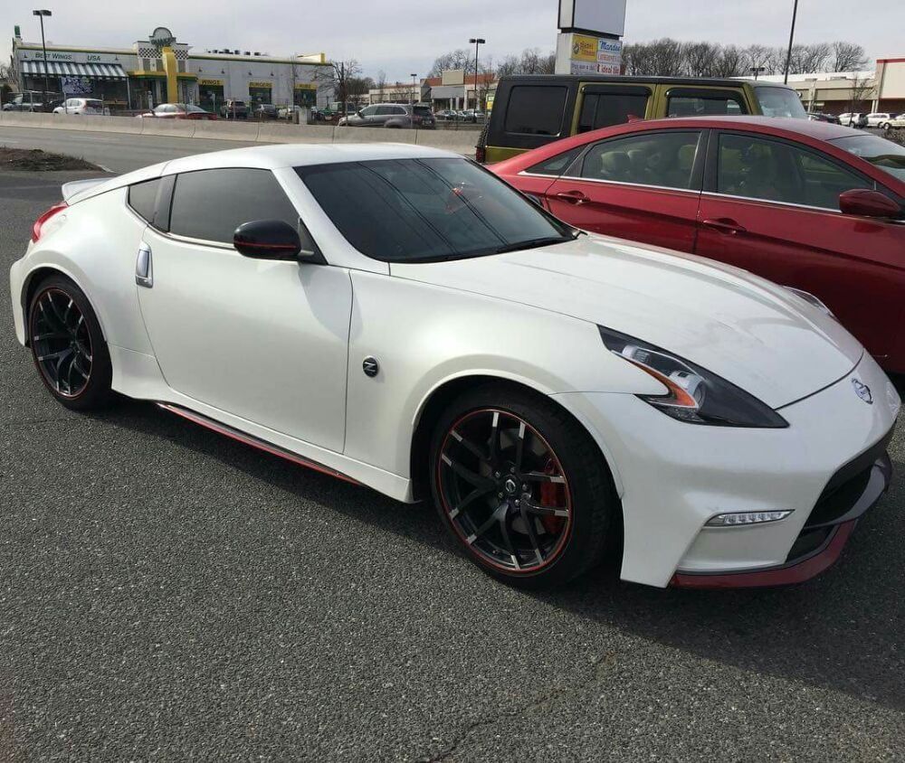 A white sports car is parked next to a red car in a parking lot.