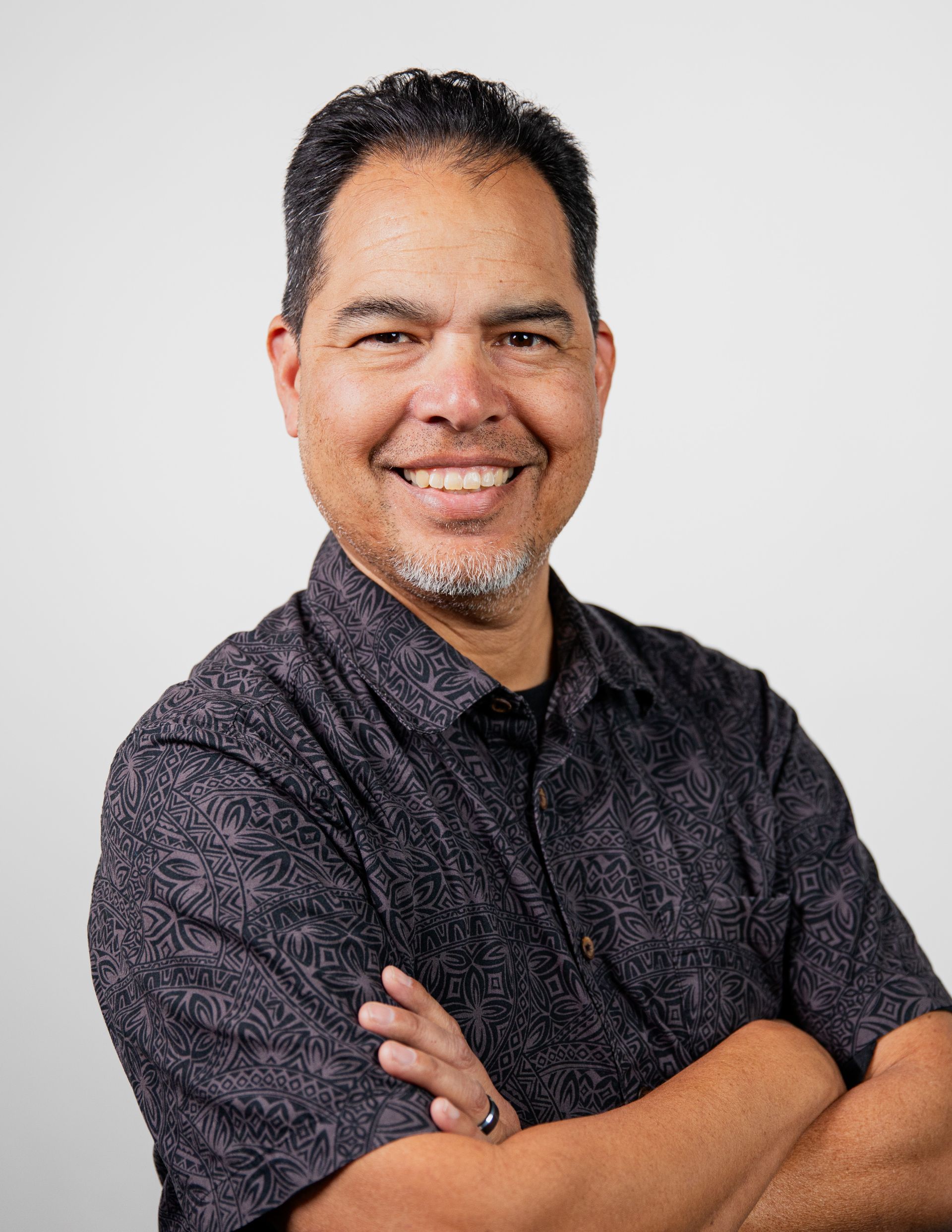 A man in a black shirt is smiling with his arms crossed.