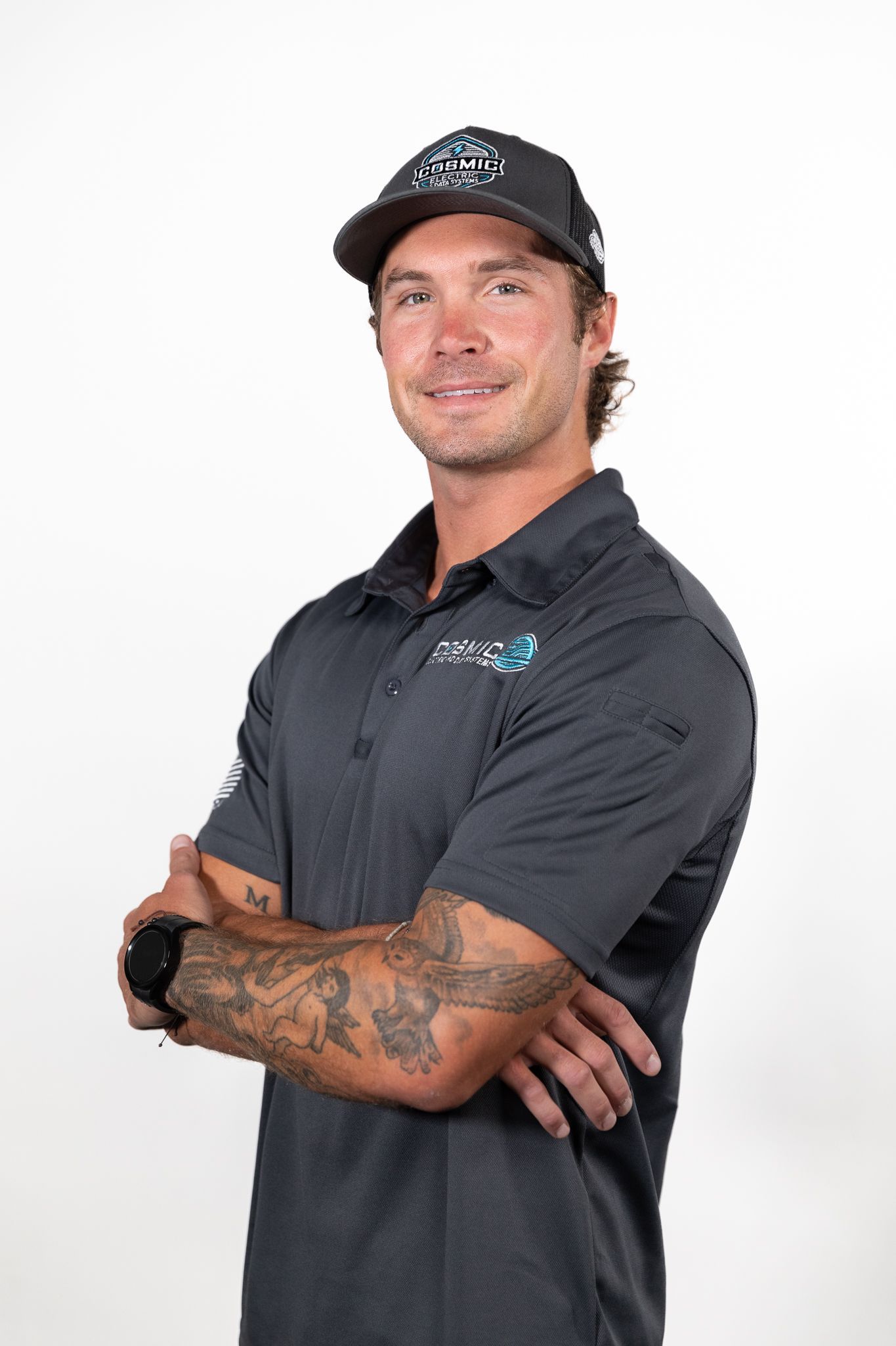 A man wearing a black hat and a grey shirt is standing with his arms crossed